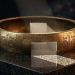 Реалистичное фото металлического зодиакального кольца на гранитной плите в луче света с четкой гравировкой названия istoknews.com на ободке.