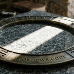 Реалистичное фото металлического зодиакального кольца на гранитной плите в луче света с чёткой гравировкой названия istoknews.com на ободке.