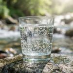 Стеклянный стакан с пузырьками воды на фоне каменистого источника