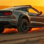 Реалистичное фото брутального спортивного фастбека Ford Mustang Baja с поднятой подвеской, массивными внедорожными шинами и двигателем V8, мчащегося по пыльной грунтовой дороге в пустыне в золотой час
