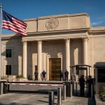 Здание посольства США в Вашингтоне с американским флагом у входа днем
