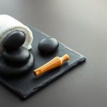 Эстетичный деревянный массажер и натуральные гладкие камни лежат на светлой поверхности.