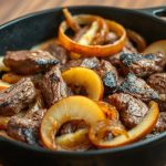 Сочные кусочки жареной печени с обжаренным луком и золотистыми дольками яблок в чугунной сковороде.