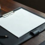 Одиночный плотный лист бумаги с печатным структурированным текстом на кожаной папке планшете.