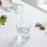 Прозрачный стеклянный кувшин с чистой артезианской водой на белой скатерти