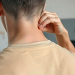 Мужчина выполняет самомассаж воротниковой зоны подушечками пальцев у основания шеи.
