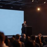 Выступление докладчика за трибуной на международном деловом технологическом форуме
