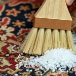 Мелкая сухая поваренная соль рассыпана по ворсу старинного шерстяного ковра с винтажным узором перед сметыванием мягкой щеткой.